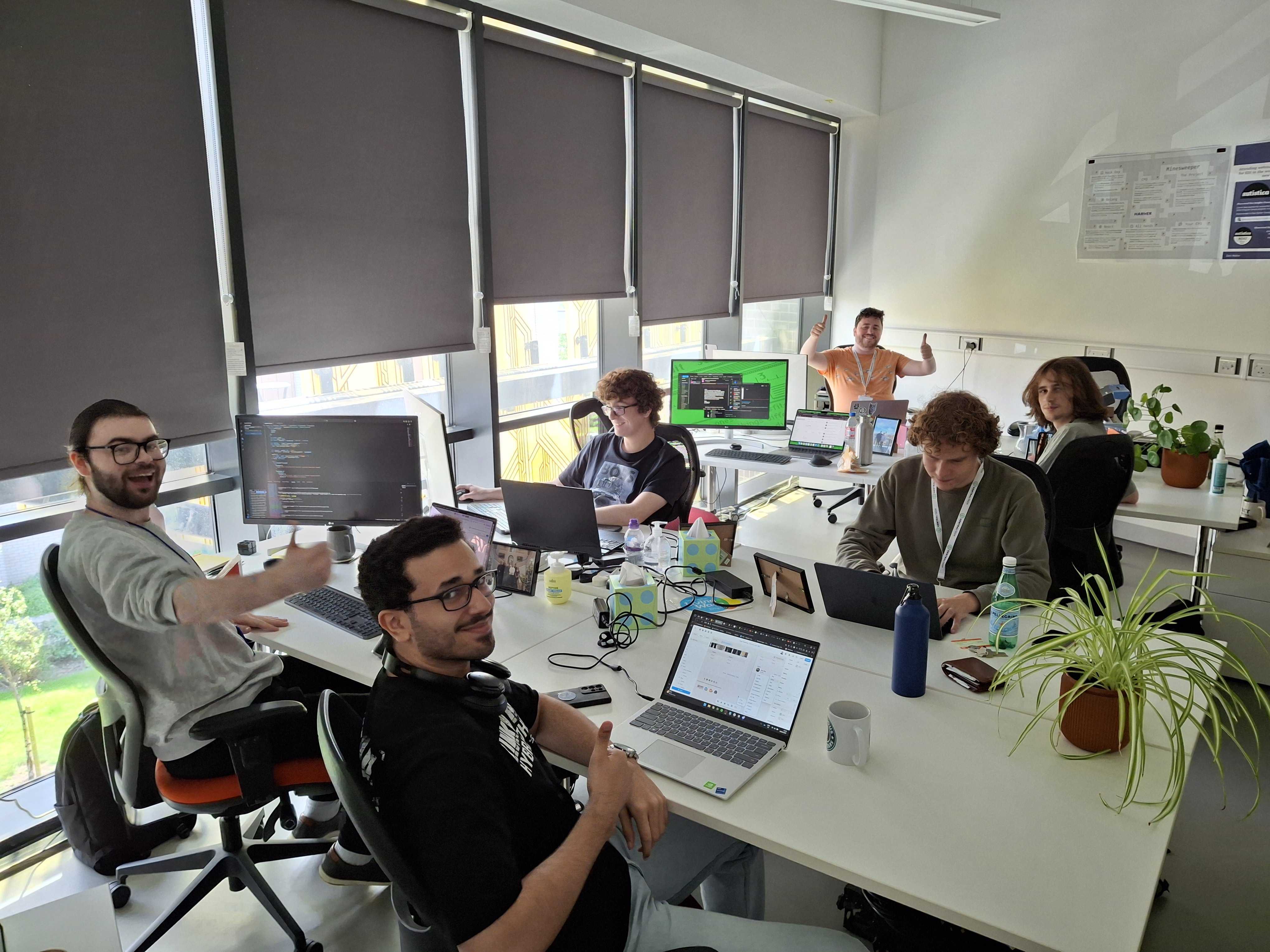 The Jamescape/Harker office room with six staff sat working at desks, some staff are smiling towards the camera.