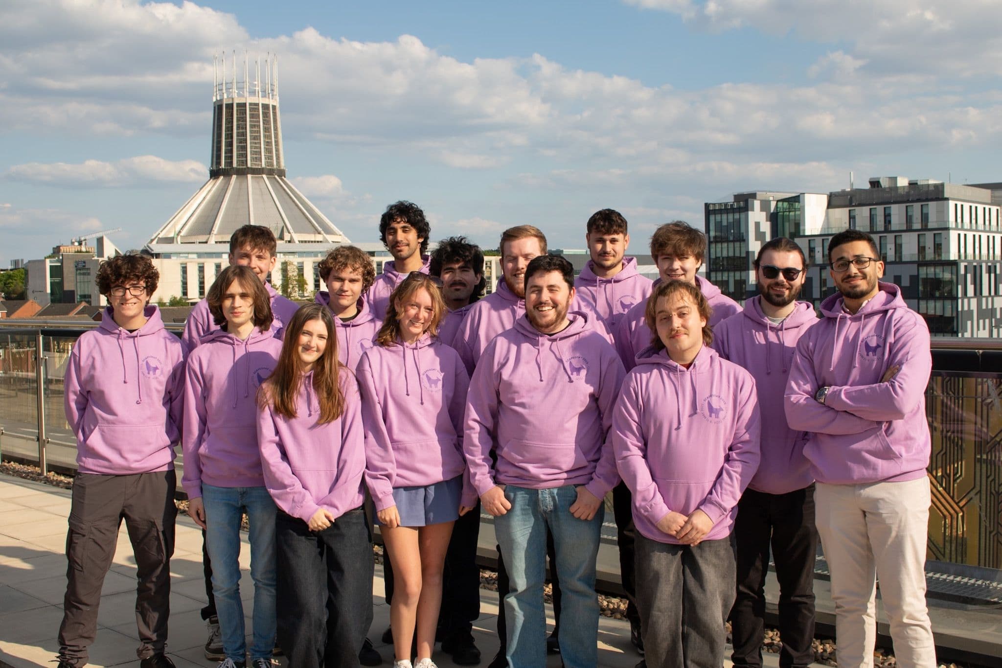 A group of Jamescape and Harker staff stood together on a roof terrace, smiling towards the camera. All staff are wearing pink Scapegoat 2025 branded hoodies.
